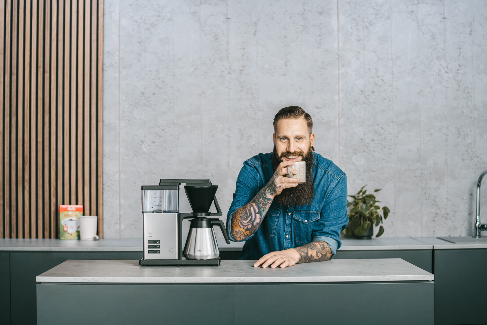 Melitta One® Therm Filterkaffeemaschine mit Isolierkanne auf einer Küchenarbeitsplatte, mit einer Person und Tasse.
