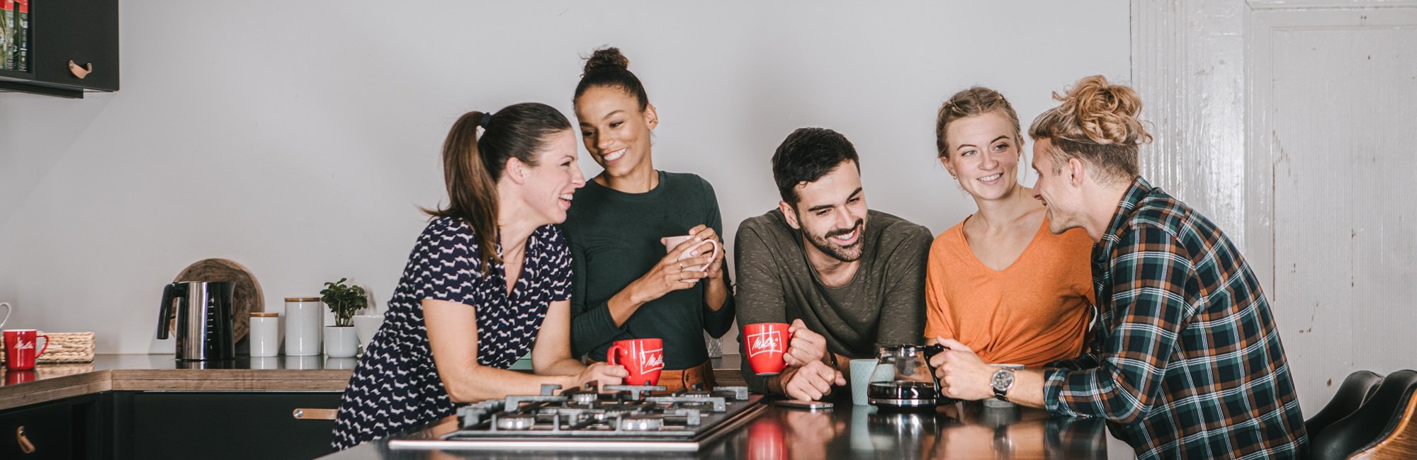 Drei Models stehen an einem Tisch, unterhalten sich und trinken einen Melitta Kaffee.