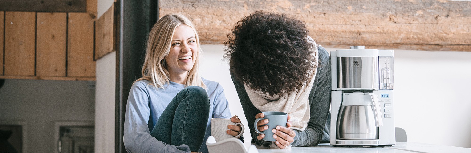 Zwei Frauen beim Kaffeegenuss neben einer Melitta Look Filterkaffeemaschine in Edelstahl