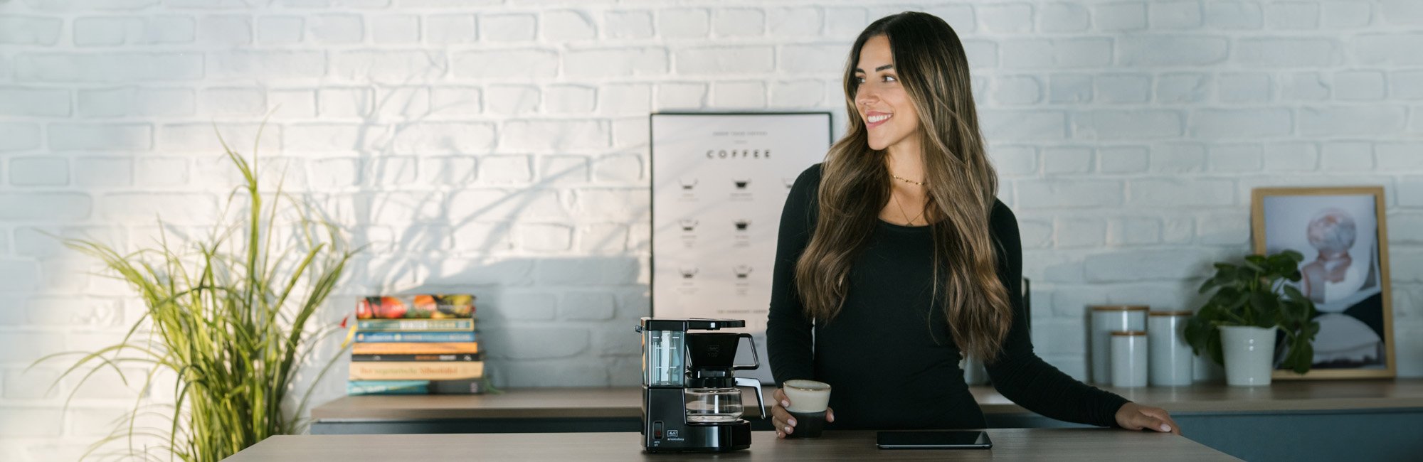In the center of the picture is an Aromaboy filter coffee machine. A woman is enjoying her filter coffee.
