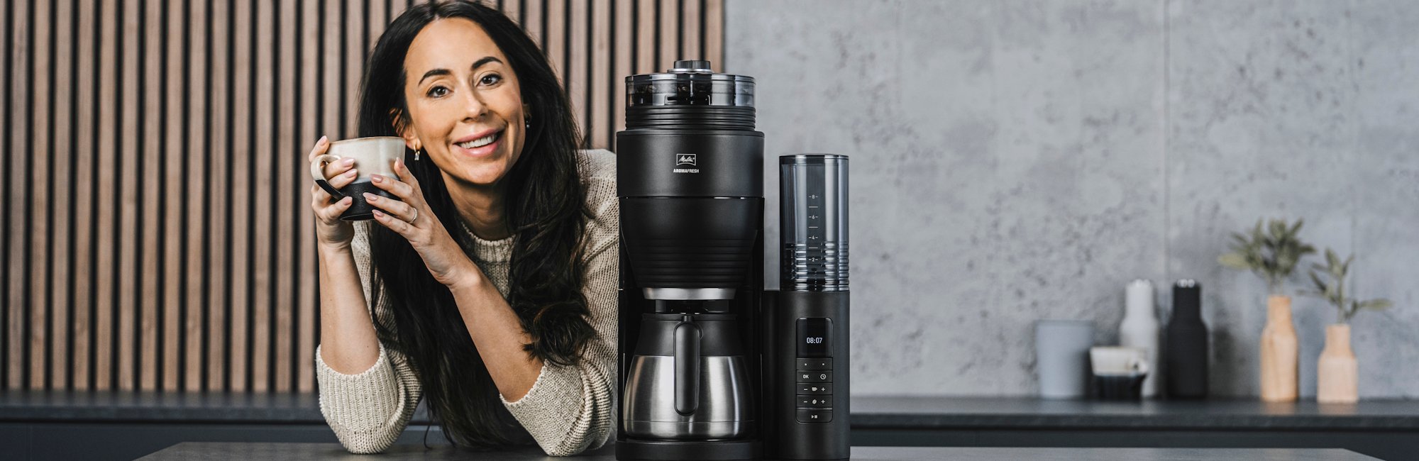 Eine Frau trinkt eine Tasse frischen Kaffee neben der AromaFresh Filterkaffeemaschine in der Küche