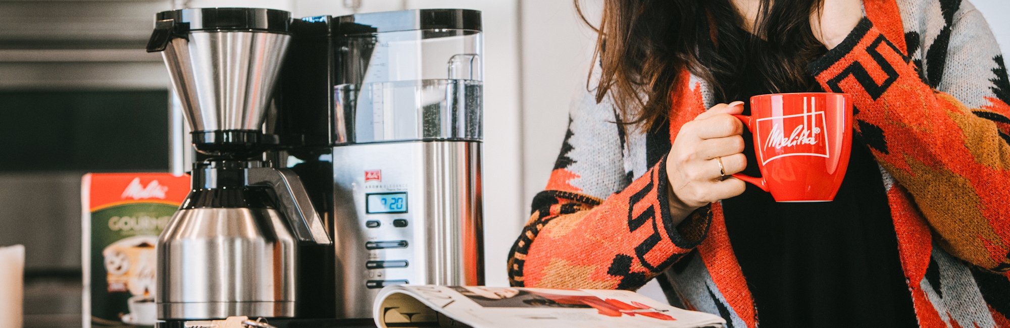 a woman drinks a Melitta coffee next to a Melitta coffee machine