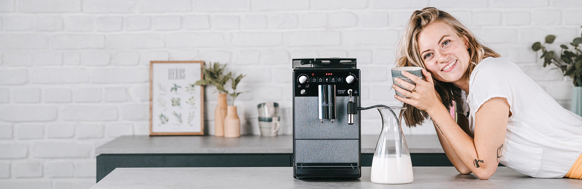 Frau in der Küche steht neben dem Melitta Avanza Kaffeevollautomaten und genießt ihren Kaffee.