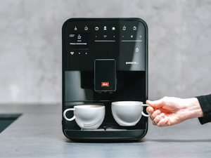 Melitta Barista steht in der Küche und eine Frau nimmt eine Tasse