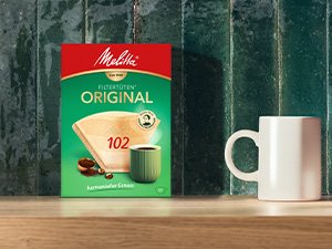 Melitta® Original 102 Kaffeefilter in der Packung neben einer weißen Tasse.