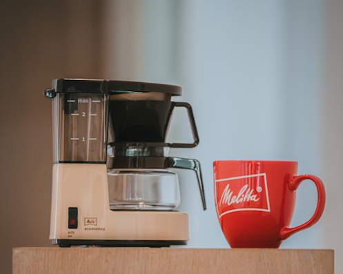Melitta Aromaboy kompakte Filterkaffeemaschine in Beige neben roter Melitta Tasse
