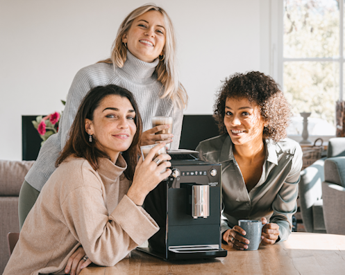 Drei Frauen sitzen neben dem Melitta Latticia OT Kaffeevollautomaten am Tisch.