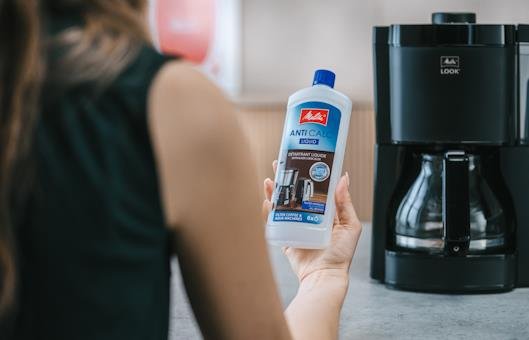 Person hält Melitta® Anti Calc Entkalker neben der Melitta® Look® Filterkaffeemaschine