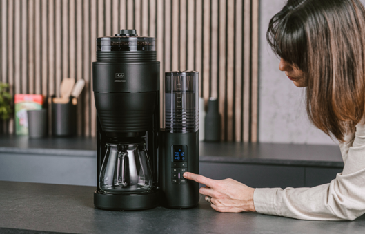 Eine Frau bedient die schwarze Aroma Fresh X Filterkaffeemaschine.