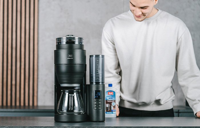 Melitta® AromaFresh X Filterkaffeemaschine mit Glaskanne und abnehmbarem Wassertank auf einer Küchenarbeitsplatte, mit Kaffeefiltern daneben